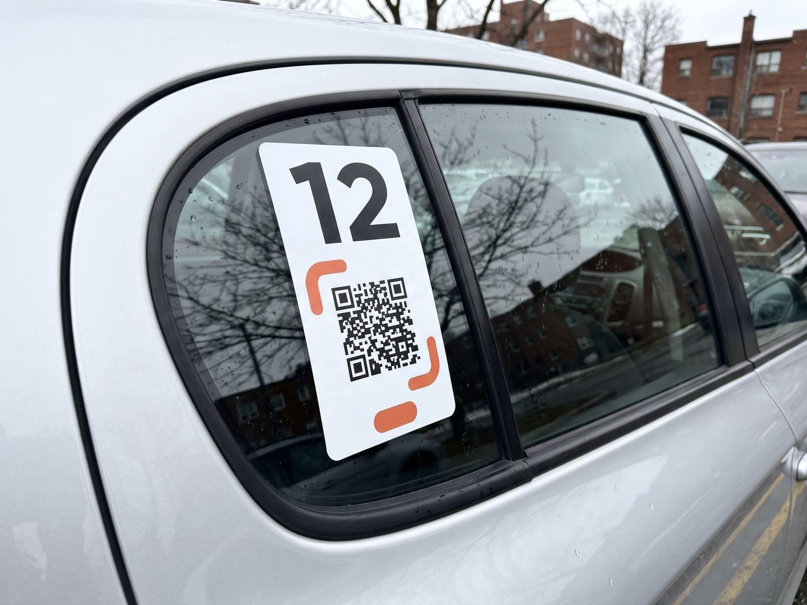A white decal with the number 12 and a QR code on the rear side window of a silver car.