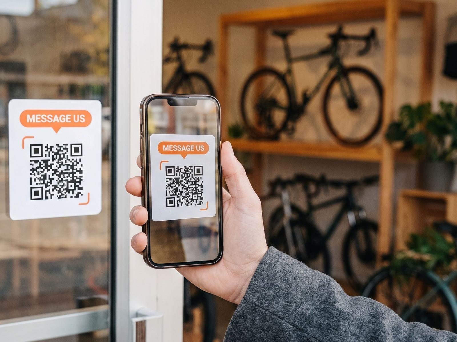 A “Message us” QR code sticker on a bike shop’s glass door, scanned with a phone from the sidewalk.