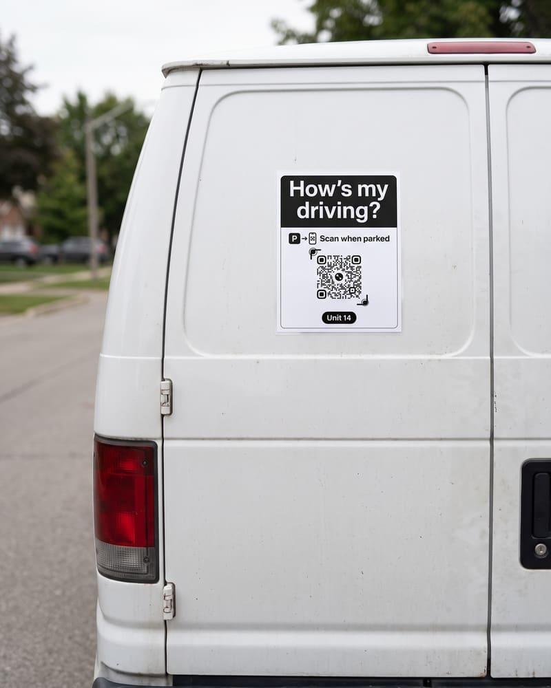 A letter-size How’s my driving sign with a QR code and Unit 14 on the back door of a white van.