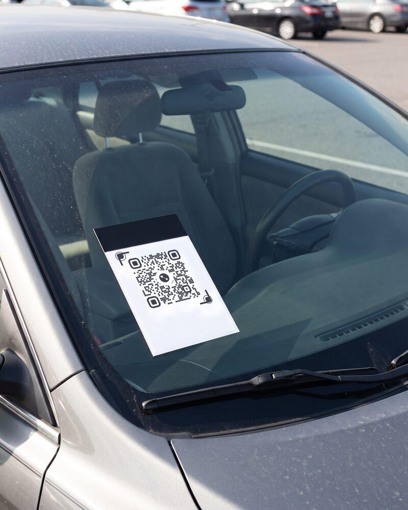 A QR card standing on the dashboard on the passenger side, leaning against the windshield, seen from outside