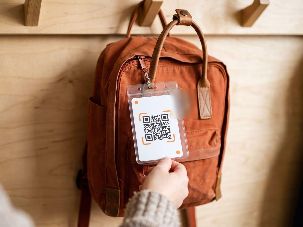 A child’s school backpack on a coat hook with an iQR code card clipped to the zipper.