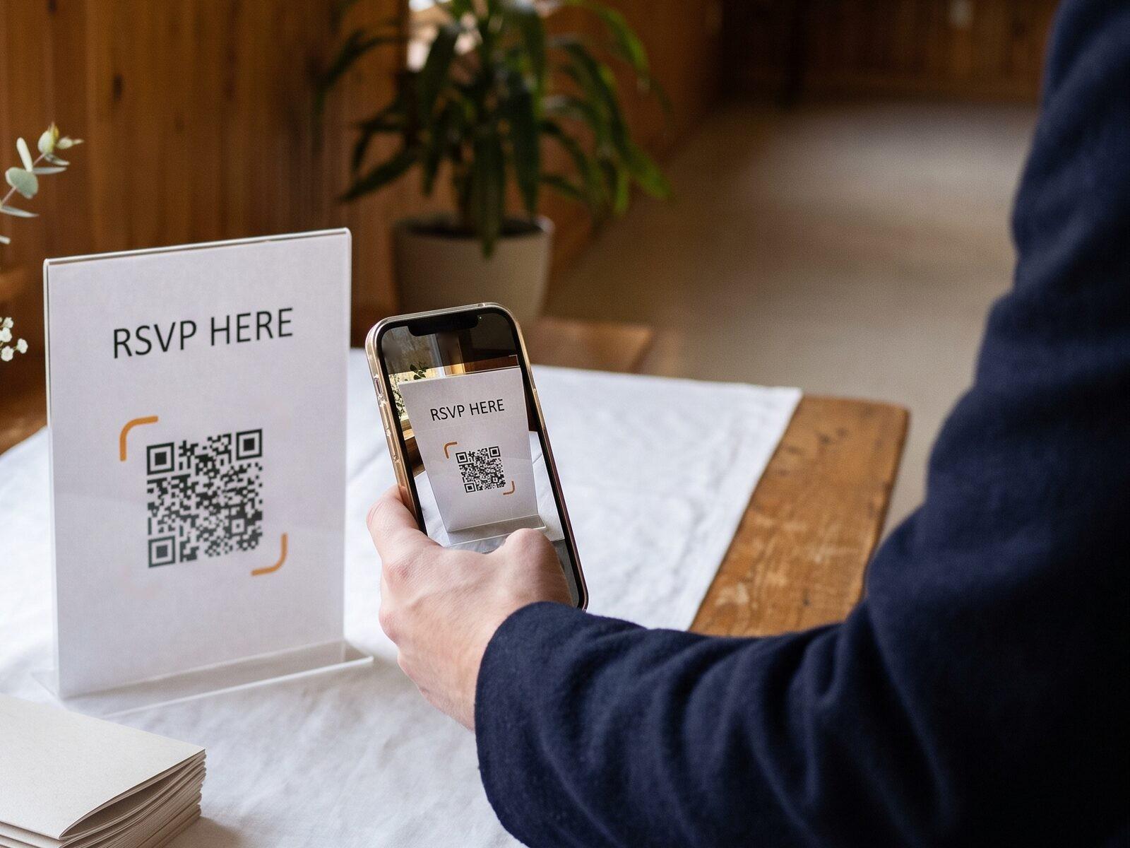 An “RSVP here” sign with a QR code on an event table, a guest scanning it with a phone