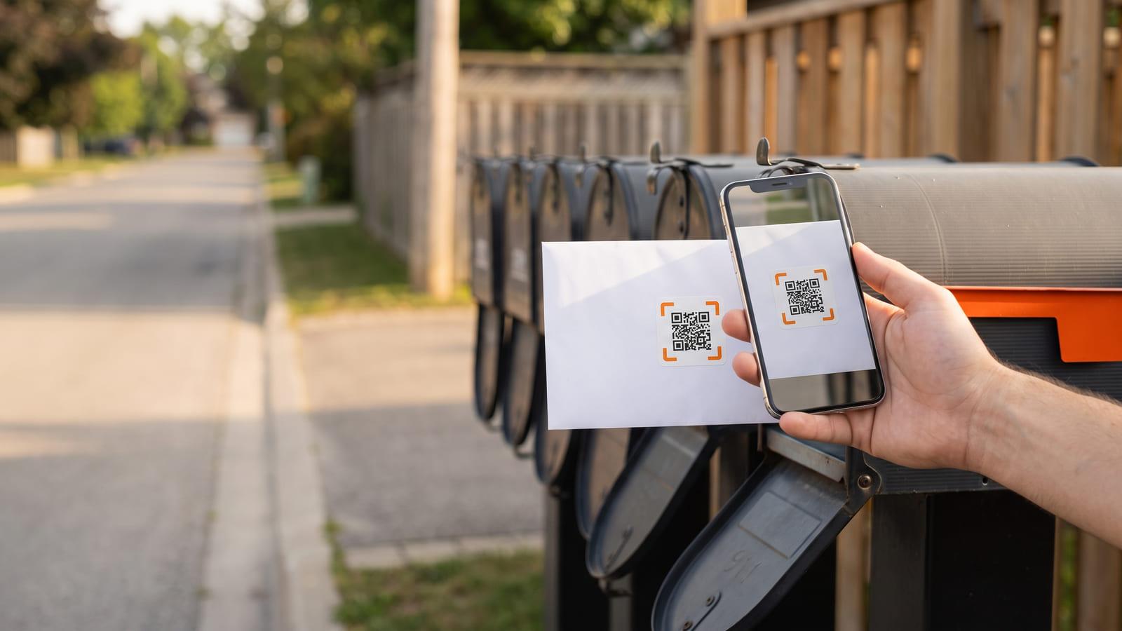A real estate farming mailer with a QR code at a row of neighbourhood mailboxes, a hand holding a phone up to scan it.