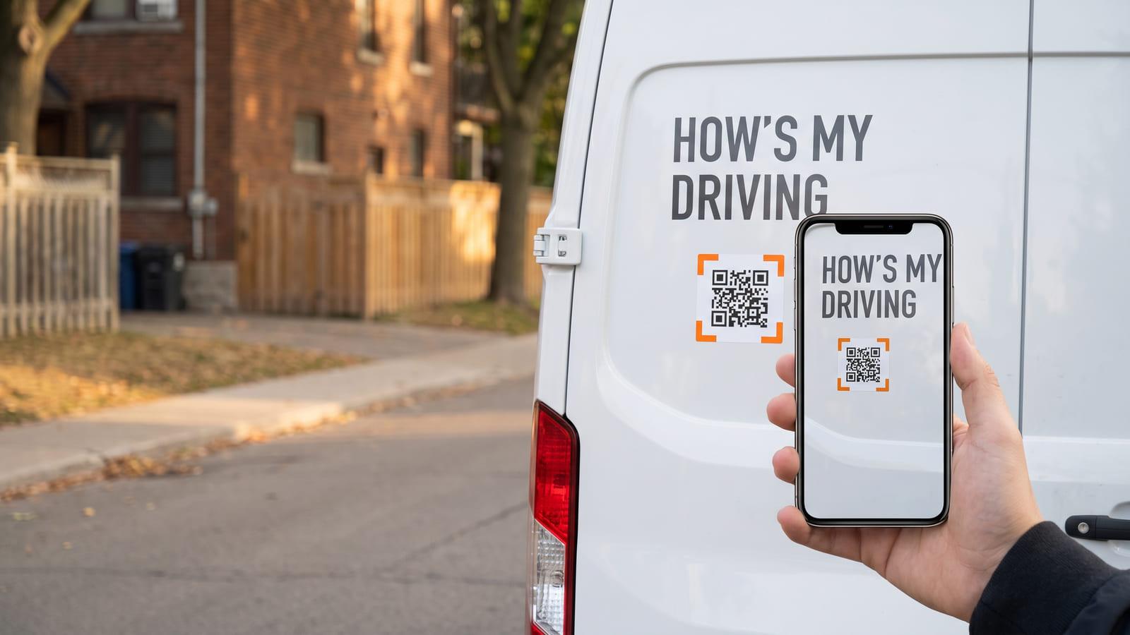 The rear door of a white van reading “HOW’S MY DRIVING” with a QR code, a phone scanning it on a residential street.